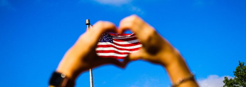 American flag seen through a heart made from two hands meeting