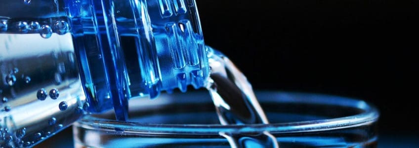 bottle pouring water into glass cup