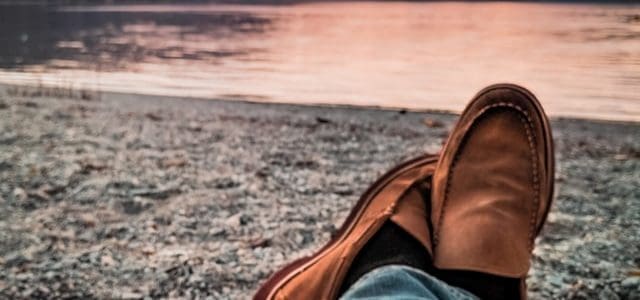 person sits on rocky shoreline