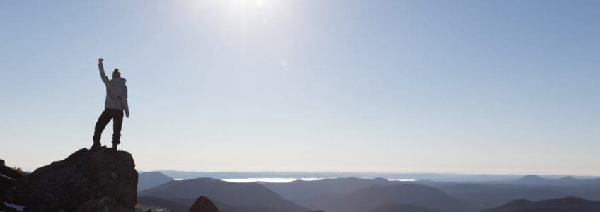 woman holds fist in the air at a mountain summit