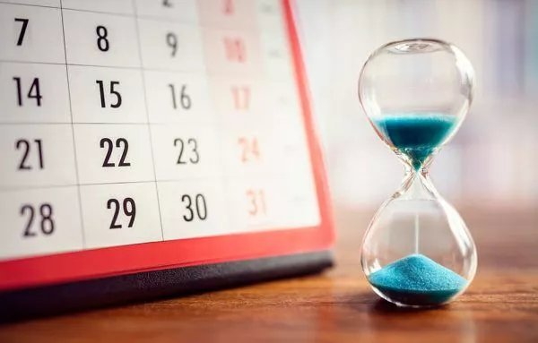 hourglass with blue sand sits by calendar