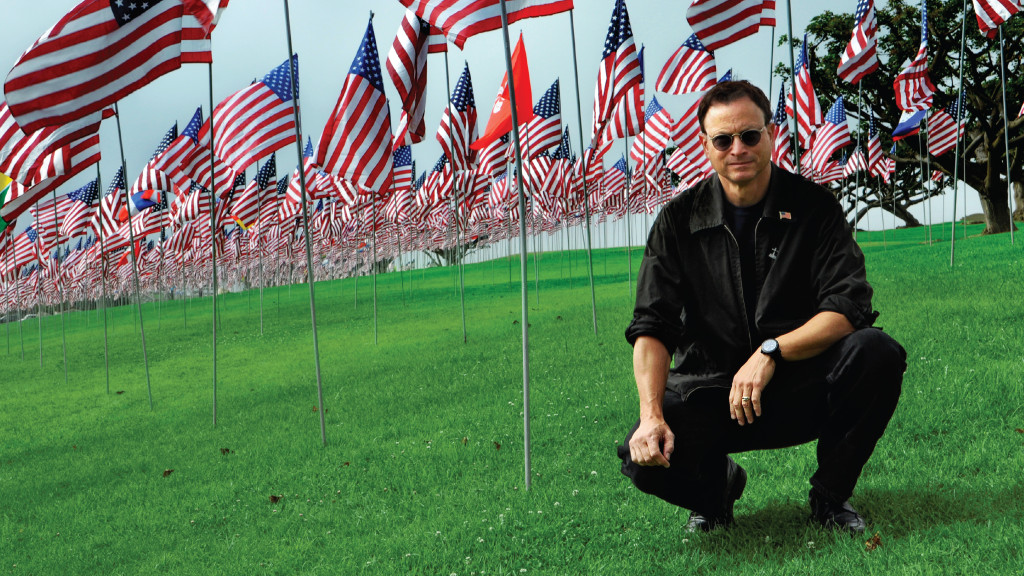 Gary Sinise crouching by American flags
